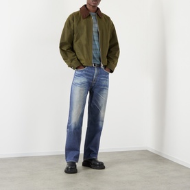 Model wearing Our Legacy Azure Print jeans in a straight-leg fit, styled with an olive jacket, denim shirt, and black loafers.