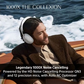 Model wearing white over-ear noise cancelling headphones, relaxing on a boat, styled with a brown jacket