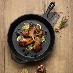 Tramontina cast iron skillet pan in black with roasted chicken drumsticks, lemon slices, and fresh herbs on a wooden surface.