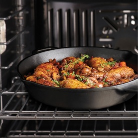 Tramontina cast iron pan in oven with roasted chicken pieces, herbs and vegetables, shown on oven rack