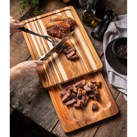 Tramontina Natural Teak Serving Board set styled with sliced meat being carved, on a rustic wooden table with oil and pepper mill.