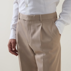 Model wearing Zegna Formal Slim-Leg Trousers in light taupe, styled with a white shirt, showing front pleats and belt loops.