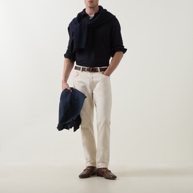 Model wearing Zegna navy cotton polo with draped scarf, carrying navy jacket, styled with cream trousers and brown loafers