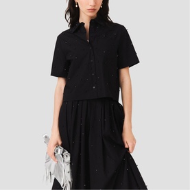 Model wearing Maje red short-sleeve embellished shirt, styled with black midi skirt and silver clutch bag