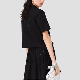 Model wearing Maje red top with scattered embellishments, styled with black midi skirt and silver clutch bag