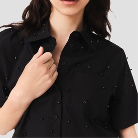 Model wearing Maje red short-sleeve shirt with scattered crystal embellishments, close-up view showing collar and button placket detail