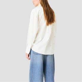 Model wearing Maje metallic white long-sleeve shirt with scattered embellishments, styled with wide-leg light wash jeans, back view
