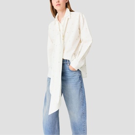 Model wearing Maje metallic white longline shirt with chest pockets, styled with blue wide-leg jeans