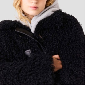 Model wearing Maje black curly shearling coat with black toggle fastening, styled with grey high-neck underlayer