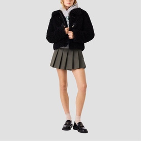 Model wearing Maje red womenswear piece styled with black faux fur jacket, khaki pleated mini skirt, and black loafers