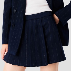 Model wearing Maje navy pinstripe pleated mini skirt with matching blazer and white top