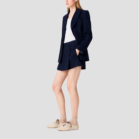 Model wearing Maje navy blazer and matching tailored shorts, styled with a white top and beige lace-up trainers