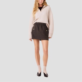 Model wearing Maje dark brown mini skirt with elasticated waist and side pockets, styled with a cream half-zip sweatshirt and black ballet flats