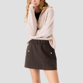 Model wearing Maje dark brown mini skirt with pearl-style button details, styled with a light pink ribbed half-zip sweater.