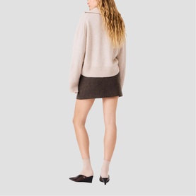 Model wearing Maje dark brown mini skirt, rear view, styled with a blush knit jumper and black kitten heel mules