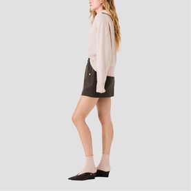 Model wearing Maje dark brown mini shorts with gold-tone button details, styled with a light pink long-sleeve top and mules.