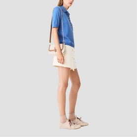 Model wearing Maje blue polo top and cream mini skirt, styled with beige lace-up flats and ankle socks