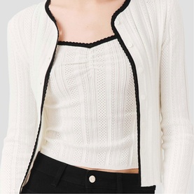 Model wearing Maje cream knit cardigan with black trim detailing, styled over a matching knit camisole with black trousers