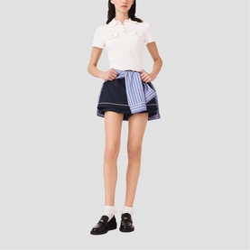 Model wearing Maje mini skirt in navy blue patchwork stripe design, styled with white polo shirt and black loafers