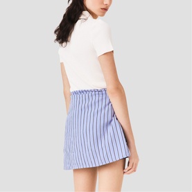 Model wearing Maje metallic blue and white vertical stripe mini skirt with white short-sleeve top, rear view