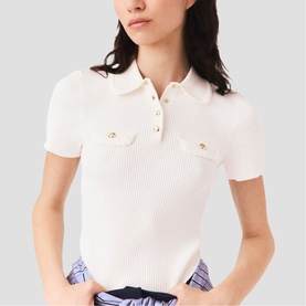 Model wearing Maje knit polo top in white with gold-tone button detail, chest pockets, and short sleeves, styled with blue printed shorts