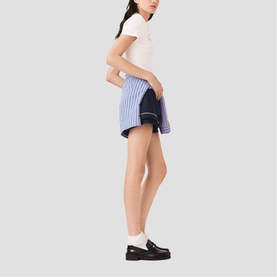 Model wearing Maje mini skirt in blue stripe and navy colourblock with white polo shirt and black loafers with white socks