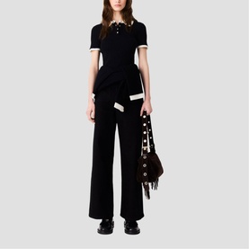 Model wearing Maje black wide-leg trousers and short-sleeve polo top with contrast trim, styled with fringed bag with stud details
