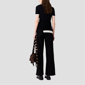 Model wearing Maje red wide-leg trousers, styled with a black short-sleeve top, carrying a studded brown bag.
