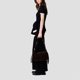 Model carrying Maje bag in dark suede with tassel and fringe details, styled with black wide-leg trousers and black loafers