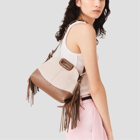 Model carrying Maje Disc Dump bag in black with fringe detail and brown hardware, styled with a white tank and pink trousers
