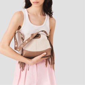 Model carrying Maje bag in beige and taupe with fringe detail, gold-tone hardware, and adjustable crossbody strap