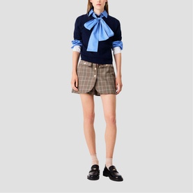 Model wearing Maje multi check mini skirt with navy bow-detail sweater and black loafers