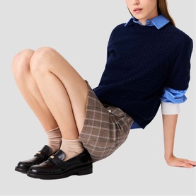 Model wearing Maje multicolour check mini skirt with navy knit sweater, blue shirt, and black loafers with ankle socks