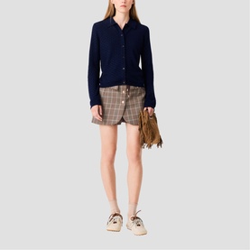 Model wearing Maje navy cardigan and multi check mini shorts, styled with a tan fringe bag and cream lace-up shoes