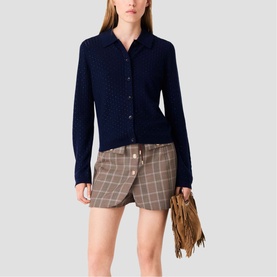 Model wearing Maje navy textured knit cardigan with collar, styled with checked mini skirt, carrying fringed suede bag