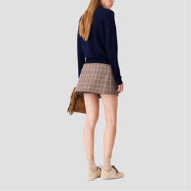 Model wearing Maje multi check mini skirt, styled with navy jumper. Rear view. Model also carries brown suede shoulder bag.