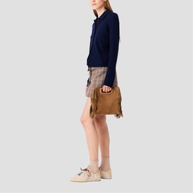 Model carrying Maje bag in tan suede with fringe detail, styled with navy knit top, checked mini skirt and cream trainers