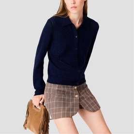 Model carrying Maje mini fringed suede bag in tan, styled with navy knit polo top and checked mini skirt