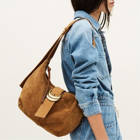 Model carrying Bash brown suede hobo shoulder bag with gold ring hardware and tan leather strap detail, styled with denim jacket