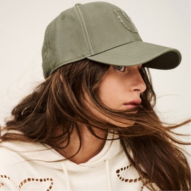 Model wearing Bash green baseball cap with small logo detail, styled with white broderie hoodie