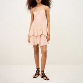 Model wearing Bash pink sleeveless mini dress with tiered ruffle skirt and V-neckline, styled with black strappy flat sandals