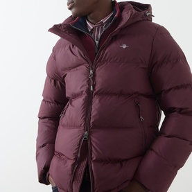 Model wearing Gant Casual Jacket in Darkened Wine, quilted puffer with hood and logo badge, styled with check shirt underneath.