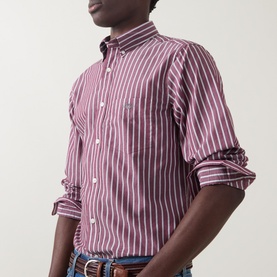 Model wearing Gant Reg Shirt in deep grape wine, bold white vertical stripes, chest pocket, rolled sleeves, styled with jeans and belt.