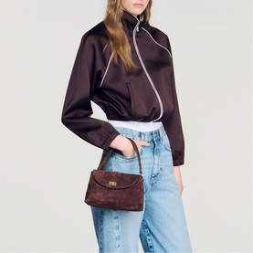 Model carrying Sandro brown suede crossbody bag with gold-tone clasp, styled with dark satin jacket and light-wash jeans