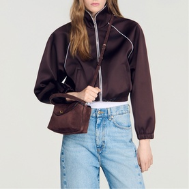 Model carrying Sandro brown leather shoulder bag with flap detail, styled with dark brown zip-up jacket and light blue jeans