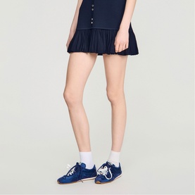 Model wearing Sandro blue suede lace-up trainers with white ankle socks and a navy pleated mini skirt.