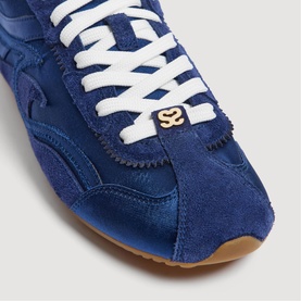 Sandro blue suede and satin trainers, close-up of toe box with gold logo badge and white laces on gum sole.