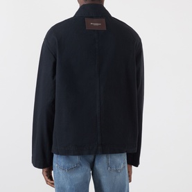 Model wearing JW Anderson black cotton casual jacket, rear view showing logo patch, styled with light blue jeans.