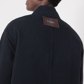 Model wearing JW Anderson black cotton casual jacket, rear view showing brown leather logo patch at collar.