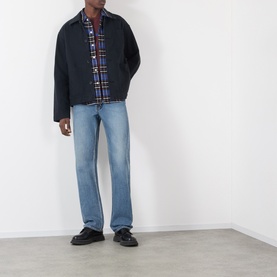 Model wearing JW Anderson black cotton casual jacket, styled with multicoloured check shirt and light blue jeans.